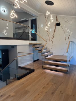 Oak floating treads with glass railing climb along a marble feature wall to a glass-railed loft with sculptural pendants.