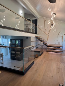 Frameless glass railing with wood handrail guards an oak floor opening and floating stair beneath a marble wall.