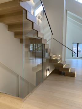 Boxy light oak Stack treads with LED step lights climb behind a full-height frameless glass guard.