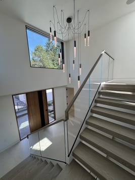 Oak floating treads with frameless glass and wood handrail turn at a landing under tall windows and glass pendants.