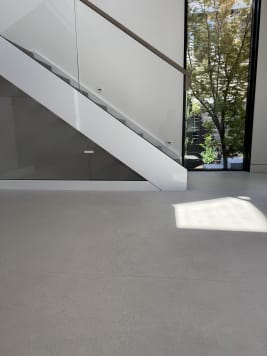 A white-stringer floating stair with frameless glass beside a tall window over a pale terrazzo floor.
