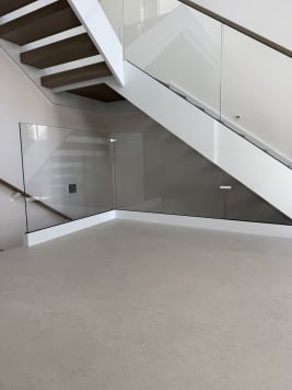 Frameless glass encloses the area beneath a white-stringer floating stair over a terrazzo floor.