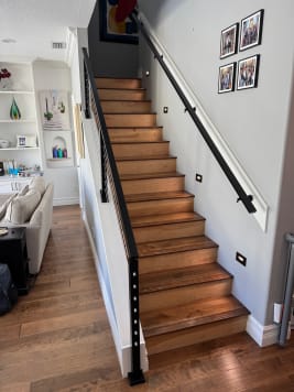 Looking up a stained wood stair with a black wall-mounted handrail and black cable railing.