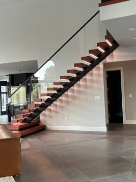 Black mono stringer floating stair with reddish wood treads, frameless glass guard and plinth steps over large-format tile.