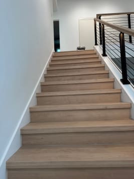 Light oak closed stair with black posts, horizontal rod infill and wood handrail along a white wall.