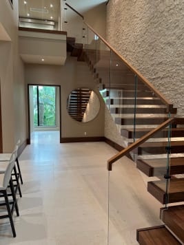 Walnut cantilever treads float off a white stacked-stone wall with frameless glass and a walnut handrail in a bright entry.