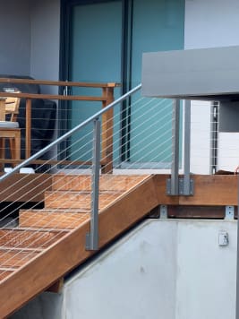 Ipe deck stair with gray mist aluminum side-mount posts and stainless cable railing beside a modern home.