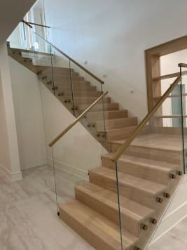 White oak stack stair with glass on brass standoff pins and a brass handrail in a bright stairwell.