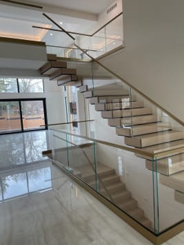 White oak stack stair with glass on brass standoff pins, brass cap rails and brass base rail above a polished marble floor.