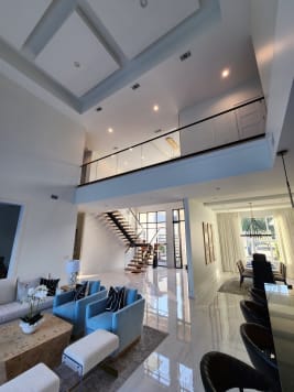 A glass railing with black cap runs along a second-floor balcony above a living room, with a mono stair beyond.