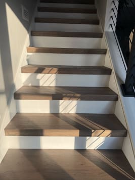 Dark oak thick-nose treads over white risers rise beside a black railing in afternoon light.