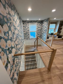 Oak newels and handrail with stainless cable infill wrap a stair opening against bold floral wallpaper.