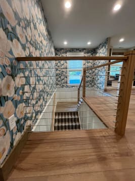 Oak newels with cable infill guarding a stair opening on a wide-plank floor.