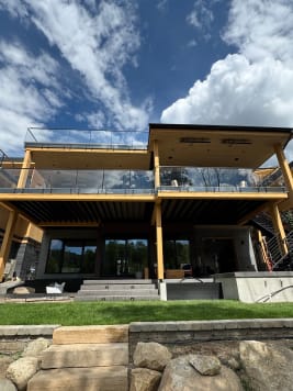 Two stacked timber-framed decks with frameless glass on black standoff pins above a landscaped lawn.