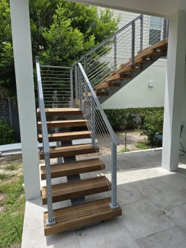 Hardwood floating treads on a mono stringer rise from a patio to an upper deck, flanked by silver-post cable railing.