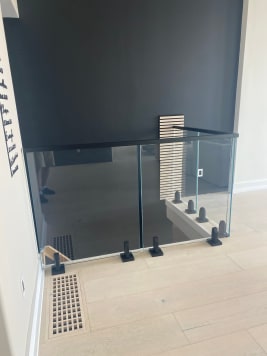 Frameless glass on black talons with a black cap guards a stair opening against a dark accent wall.