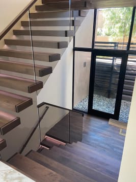 Walnut cantilevered treads turn at a landing beside frameless glass and wall handrail above a window to the garden.