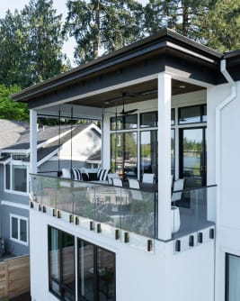 Side-mounted glass railing with talon clamps and a slim cap wraps a covered balcony on a white lake home.