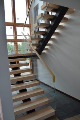 Maple floating treads on a black mono stringer with frameless glass and a maple handrail by tall windows