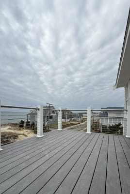 A composite deck with white posts and a stainless top rail carries horizontal cable railing overlooking a coastal neighborhood and the ocean.