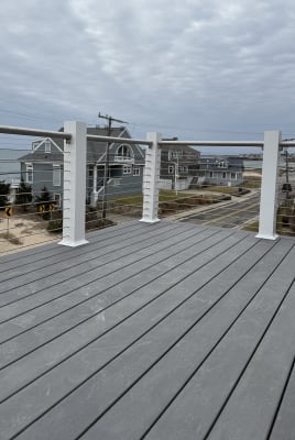 A composite deck with white posts and a stainless top rail carries horizontal cable railing overlooking a coastal neighborhood and the ocean.