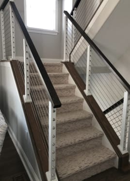 Black top rail and white posts with stainless cable infill mounted on knee walls flanking a carpeted stair.