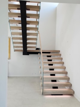 Light oak treads on a black mono stringer turning at a landing with frameless glass and LED lighting.