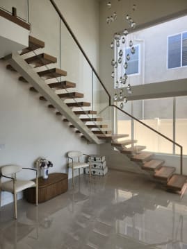 Oak floating stair with white stringer and frameless glass with wood handrail rising beside a crystal chandelier over polished marble.