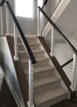 Black top rail and white posts with stainless cable infill mounted on knee walls flanking a carpeted stair.