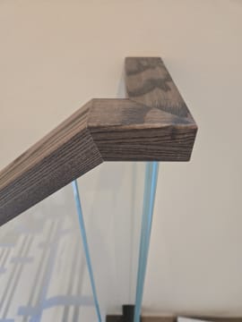Close view of a weathered oak handrail mitered on top of frameless glass