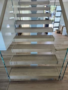 Head-on view of thick white oak floating treads between two frameless glass railings