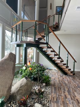 Dark stringer floating stair with wood treads and cable railing rises above an indoor rock garden.