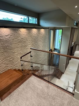 Upper landing with frameless glass and walnut handrail overlooking a stone-wall foyer.