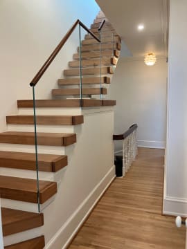 Thick wood treads with a frameless glass panel and wood handrail retrofitted onto a stair in a white hallway.