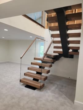 Thick wood treads on a black mono stringer rising through winders beside frameless glass with a wood handrail.