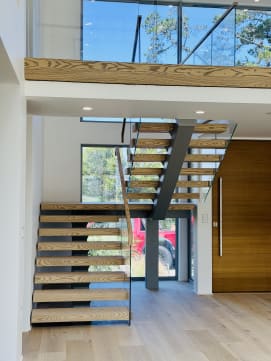 Switchback floating stair with ash treads below a wood-fascia loft, glass railing along the run