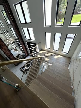 Looking down a floating stair with glass on brass talons and a gold handrail toward a marble foyer