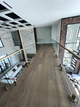 Frameless glass on brass talon spigots lines an oak-floored bridge over a living room