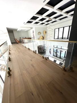 Frameless glass on brass talon spigots runs along an upper-floor balcony under a coffered ceiling