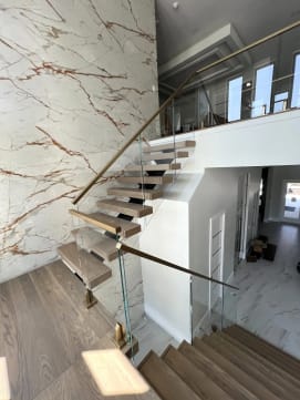 Floating oak stair with glass on brass talons and a gold handrail against a marble wall