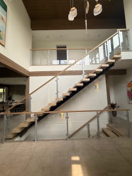 Long floating stair on a black mono stringer with glass-and-post railing and wood handrail rising to a balcony