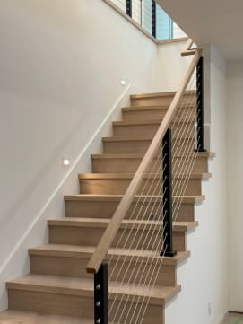 White oak stair with a black-post cable railing and continuous oak handrail