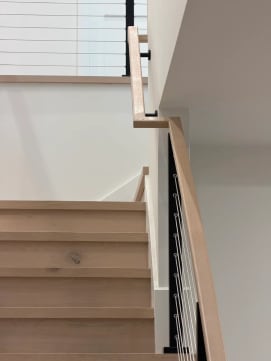 Oak stair treads with black cable railing and a white oak handrail turning at a landing