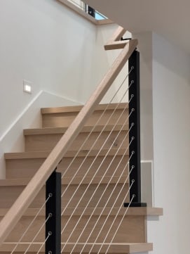 Black cable railing with white oak handrail climbing a stair of oak treads