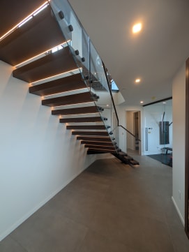 Dark walnut floating treads with LED underlighting and standoff-pin glass in a long hallway