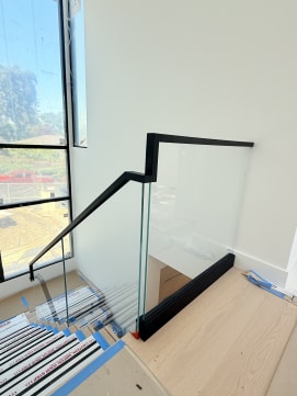 Frameless base rail glass with a black top cap turns at the head of a stair by tall windows