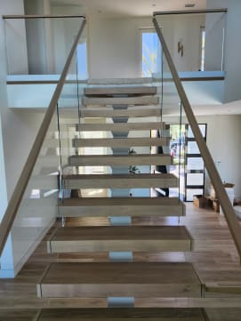 Wide white oak floating treads on a center stringer with frameless glass and oak handrails on both sides