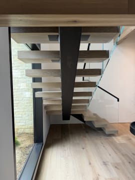 Black mono stringer with white oak floating treads and frameless glass beside a stone-clad window