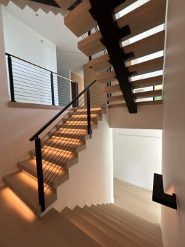 White oak FLIGHT Mono switchback with warm LED tread lighting and black horizontal cable railing