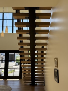 White oak floating treads on a dark mono stringer seen from below in a bright entry